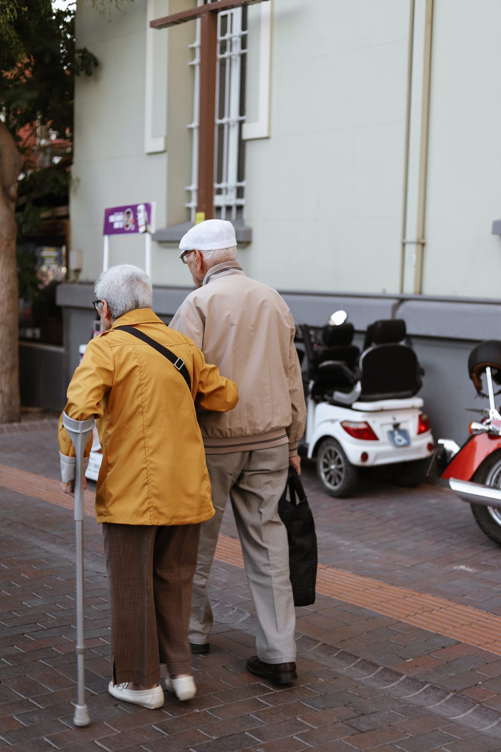 Elderly couple walking down the street, and the woman is using an arm cane.